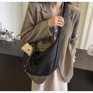 Detail of black pebbled leather hobo bag with teddy charm on a khaki blazer