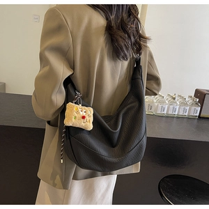 Detail of a black leather hobo bag with a plush bear charm on a female model's shoulder