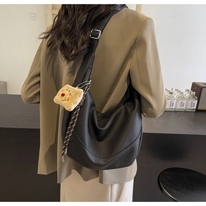 Detail of black pebbled PU leather crescent bag featuring a cute plush toast charm