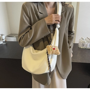 Detail of creamy white crescent bag with lychee leather texture and plush charm