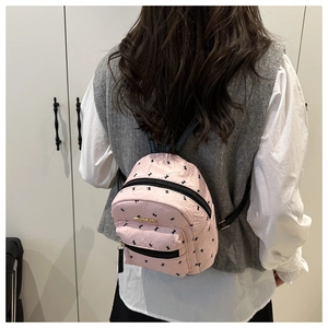 Close-up of small pink backpack featuring black bow patterns and gold logo detail