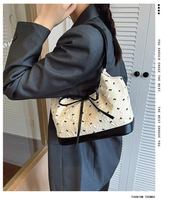 Detailed view of white pleated handbag with black bow patterns and elegant ribbon detail