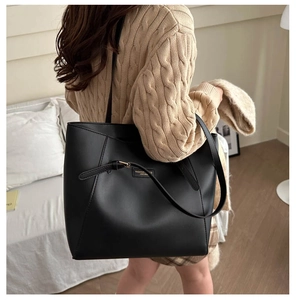Close-up of a large black leather tote bag with gold buckle details on a model