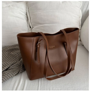 Detail of a brown leather tote bag with embossed logo on a white sofa in a cozy room