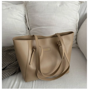 Detail view of khaki PU leather tote bag with vertical stitching on a white sofa