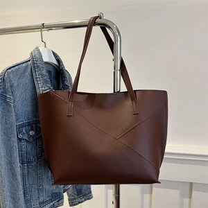 Large dark brown leather tote bag with geometric stitching hanging on a minimalist display