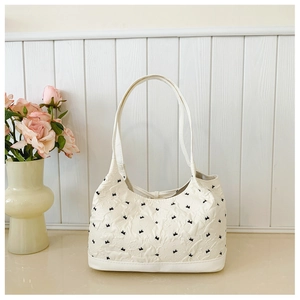 Detail of creamy white tote bag with black bow embroidery and wrinkled fabric texture