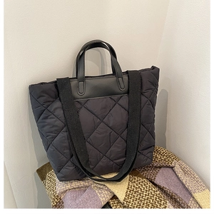 Detailed view of stylish black quilted tote bag with rhomboid pattern and dual strap design.
