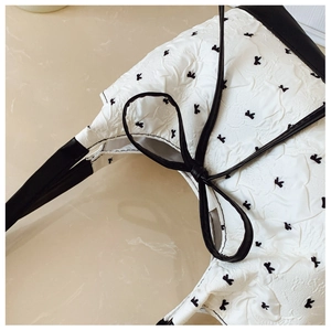Close-up of pleated white fabric tote bag with black bow print and leather trim details