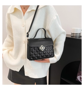 Detail of a black quilted crossbody bag with a gold petal twist lock and top handle