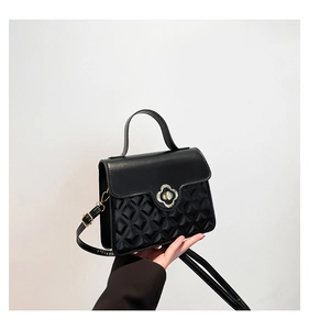 Detail showing hand holding a black quilted square crossbody bag with clover lock