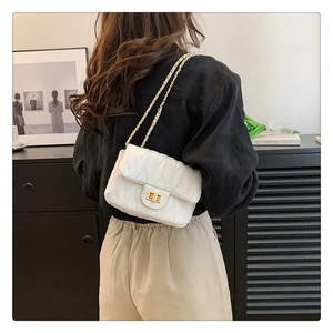 Modern white quilted shoulder bag with gold metal clasp shown on female model shoulder