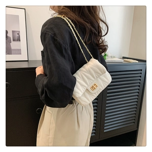 Close-up of white quilted chain bag with V-shaped stitching and gold twist lock clasp