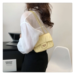 Side view of a quilted light yellow crossbody bag with gold chain strap on a model