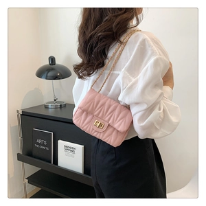 Pink pleated crossbody bag with gold chain strap worn by a model in a modern room