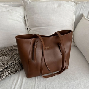 Minimalist brown large capacity leather tote bag for daily commuting on white sofa
