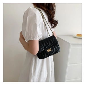 Detail of black quilted shoulder bag with gold twist lock and woven chain strap