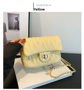 Detail of yellow quilted chain bag with gold rotating lock and V-stitch pattern on faux leather
