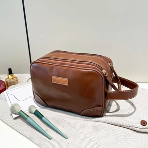 Brown faux leather cosmetic bag with double zipper and side handle on textured fabric
