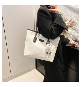 Detail of cream tote bag with fine embossed texture, brown handles and plush ball charm