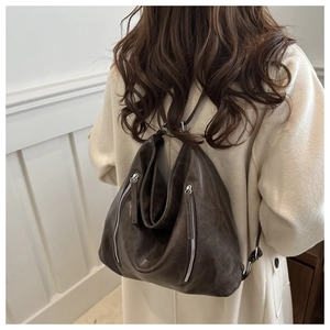 Close-up of a large vintage brown leather tote bag with side zipper on a beige coat