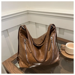 Detail of vintage brown PU leather tote bag with vertical zippers on a wooden table