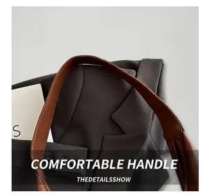 Detailed close-up of brown leather bag handle with fine stitching on a grey blazer