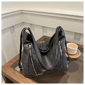 Detail of a large black leather tote bag with silver zippers on a coffee table