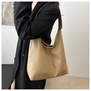Close-up of a large khaki hobo bag with litchi grain texture worn by a model in a suit