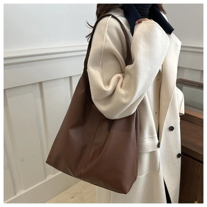 Close-up of brown pebbled leather tote bag with vertical stitching on a cream coat