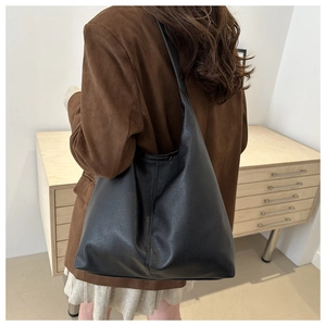 Close-up of black lychee grain leather tote bag worn by model in a minimalist setting