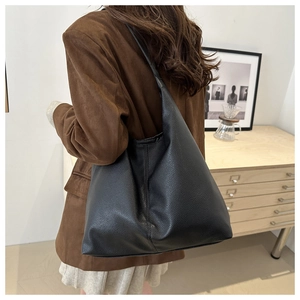 Close-up of a large black pebbled leather tote bag worn with a brown blazer jacket