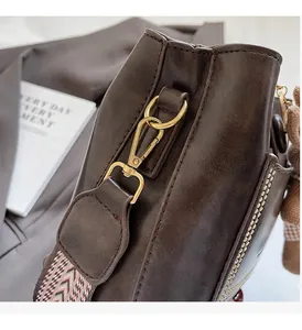 Detalle de bolso cubo marrón oscuro con herrajes dorados y correa geométrica