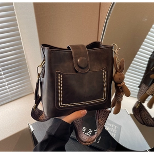 Detalle de bolso cubo marrón vintage con remaches dorados y correa de tejido