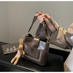 Detalle de bolso tipo cubo de cuero marrón con correa jacquard y dije de conejo