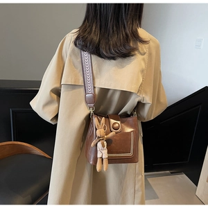 Detalle de bolso cubo en cuero marrón con pespuntes y bandolera tejida de estilo étnico