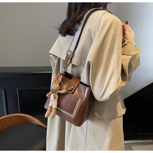 Detalle de un bolso cubo de cuero marrón con un amuleto de conejo y correa tejida de moda
