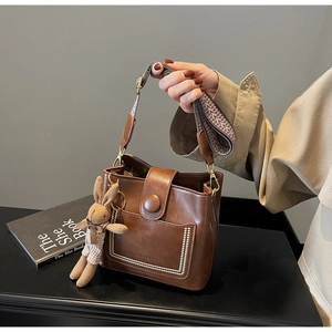 Detalle de bolso cubo marrón con correa tejida y colgante de conejo de cuadros