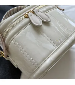 Detail of creamy white textured box bag featuring gold hardware and a branded strap