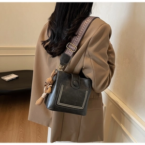 Detalle de bolso tipo cubo de cuero negro con bolsillo de perlas y asa estampada