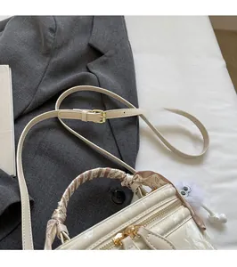 Detail of cream box bag with silk scarf on handle and adjustable gold buckle strap