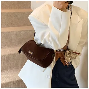 Close-up of brown suede hobo bag with gold Fashion logo paired with white blazer