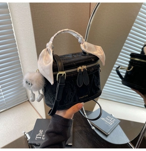 Detail of black cylinder box bag with gold zipper, silk scarf handle, and plush charm