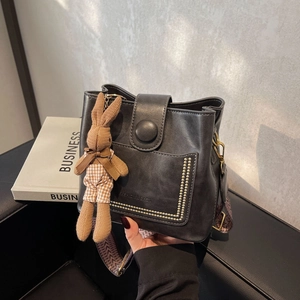 Detalle de bolso cubo negro con costuras de remaches y colgante de conejo de peluche