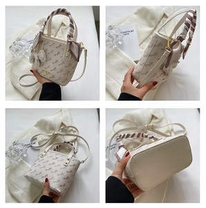 Detail view of cream bucket bag with carriage print, silk scarf handle and golden hardware
