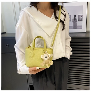 Detail of yellow lychee leather bucket bag with a cute bear charm for summer styling