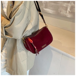 Detail of burgundy crossbody pillow bag with gold hardware and leaf pendant charm