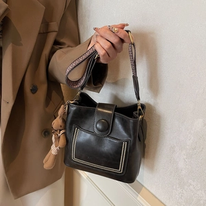 Detalle del bolso de cubo negro en cuero con correa geométrica y colgante de oso