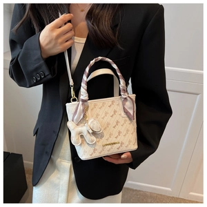 Detail of cream crossbody bag with vintage horse pattern, silk scarf, and dog charm