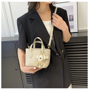 Detail of beige lychee pattern bucket bag with cute bear charm and thin shoulder strap